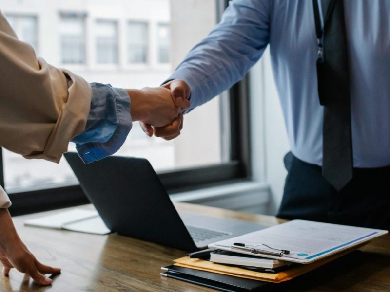 pexels-photo-5673488-5673488 Crop unrecognizable coworkers in formal wear standing at table with laptop and documents while greeting each other before meeting